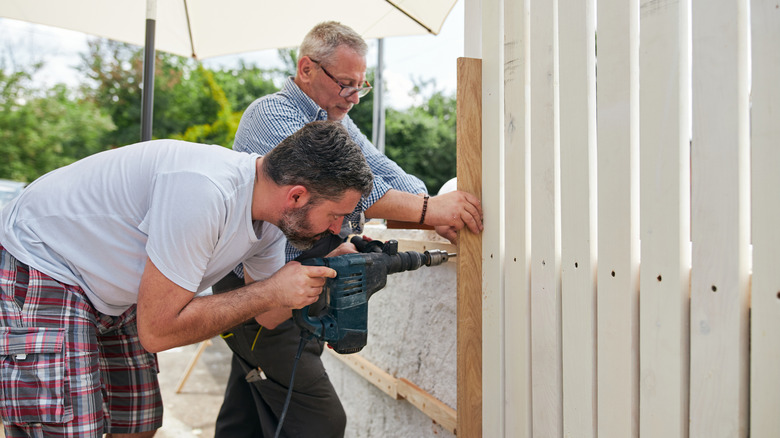 two people using a drill to build a fence