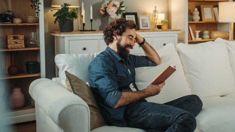 A person sits on couch, reading a book in the living room
