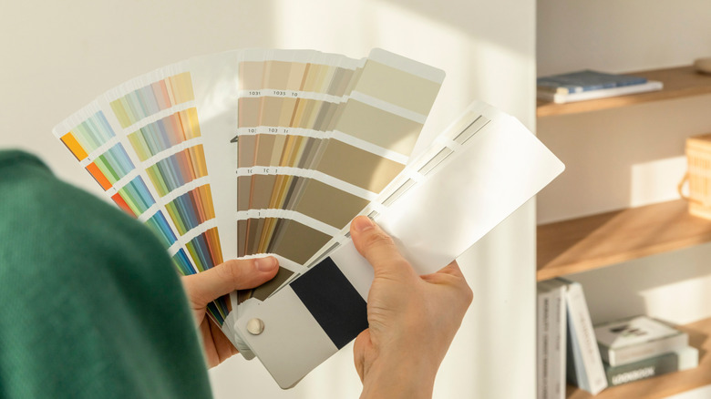 A person in a green shirt looking at a thick book of paint swatches with a white wall and a wooden bookshelf in the background