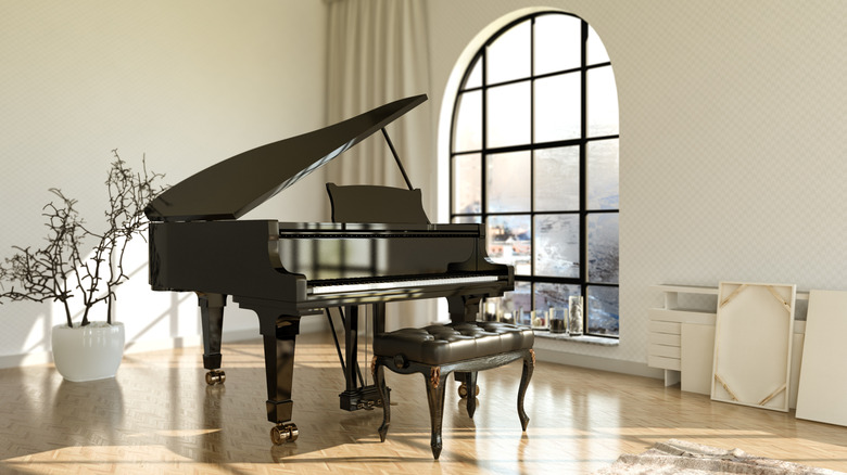 dark grand piano and stool in a light room with pale flooring, arched window with dark bars and a plant