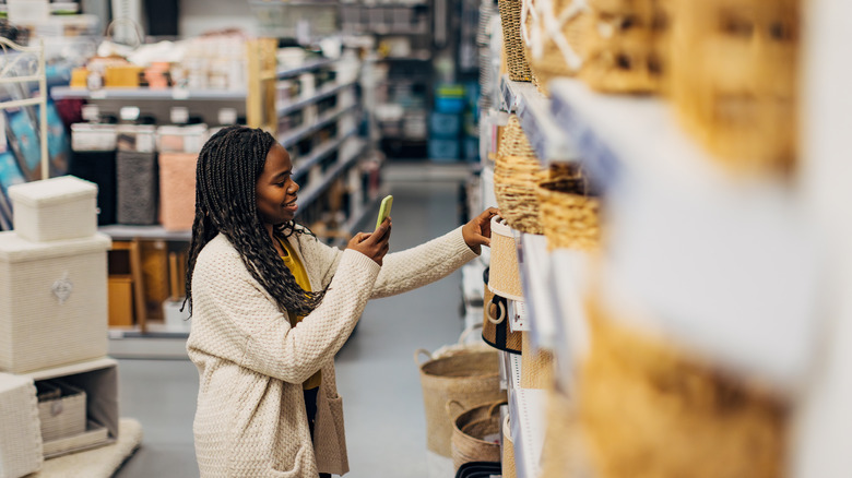A smiling woman looks at her phone while shopping for IKEA baskets.