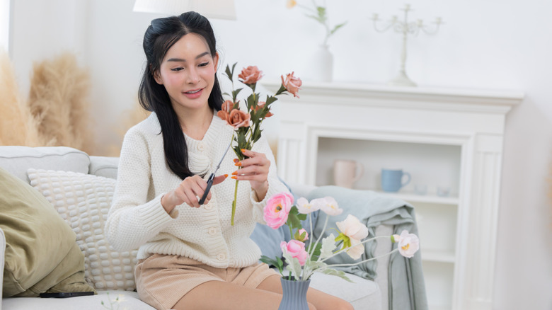 Woman cutting fake flowers while sitting on a sofa