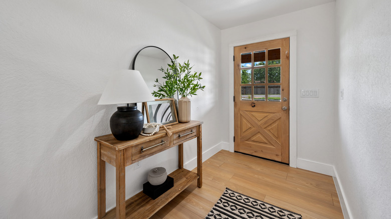 A modern entryway with a wooden sideboard, a black lamp, a plant, and a mirror