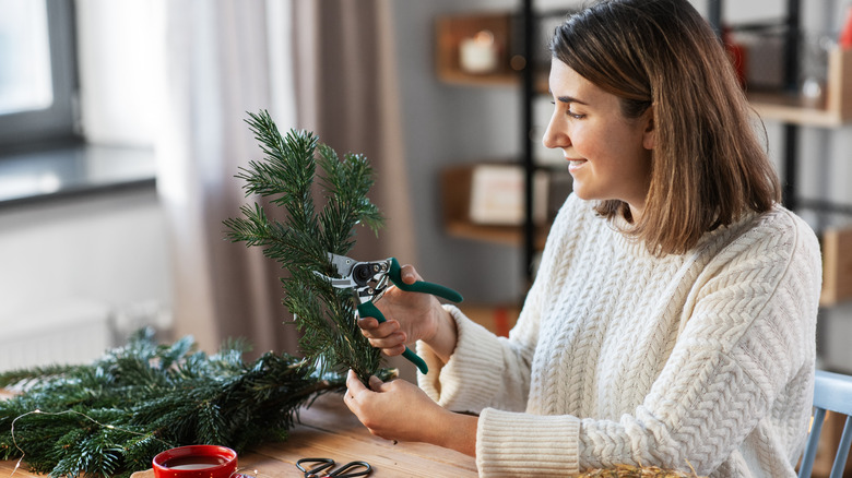 Woman cutting festive branches with pruners indoors