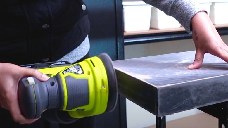 person sanding black LACK shelf with RYOBI palm sander