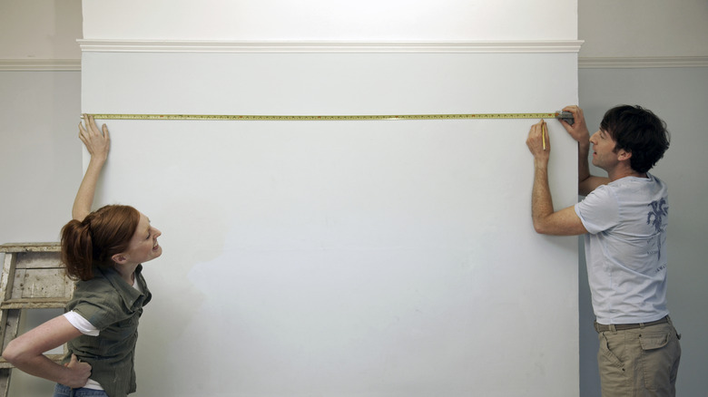 Two people measure a blank wall