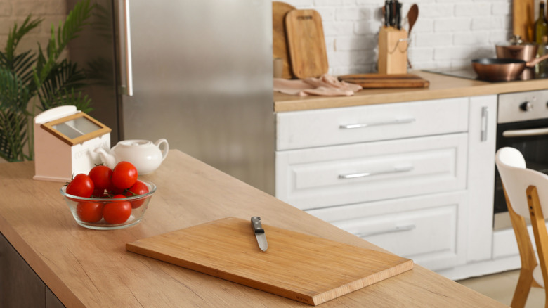 cutting board on counter next to a bowl of ripe tomatoes