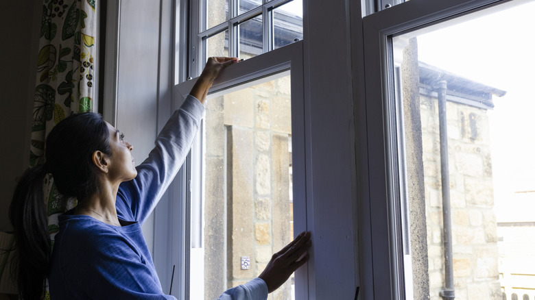 Person in blue sweater closing window.