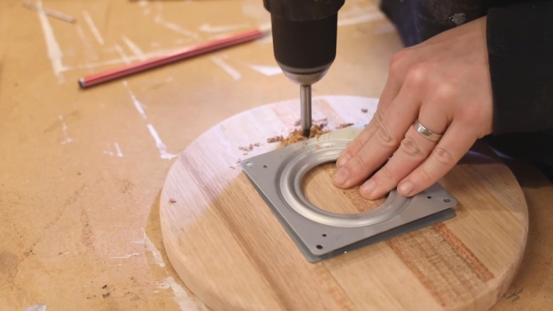 Person drilling a large access hole through a board to install a turntable