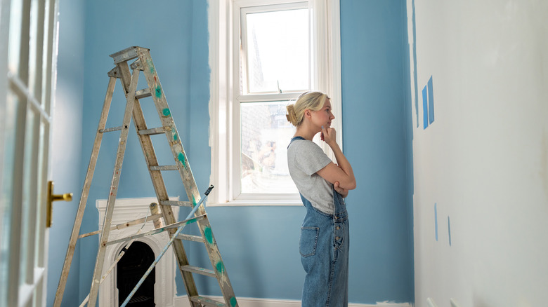 A woman looks at a blank white wall while decorating her living room