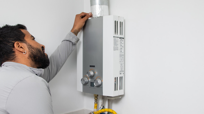 A man inspects a wall-mounted tankless water heater.