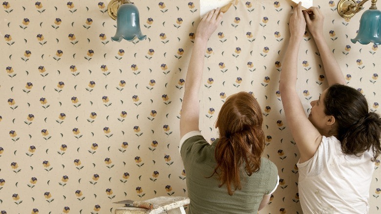 Two women removing flowered wallpaper