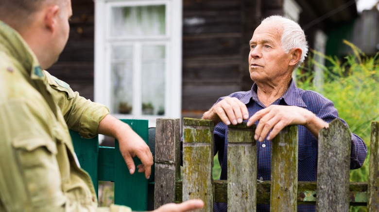 neighbors talking over old wooden fence