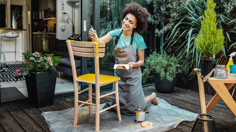 smiling young woman painting chair yellow