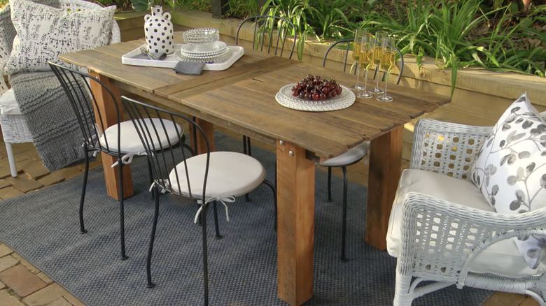 A wooden table with outdoor furniture and a rug.