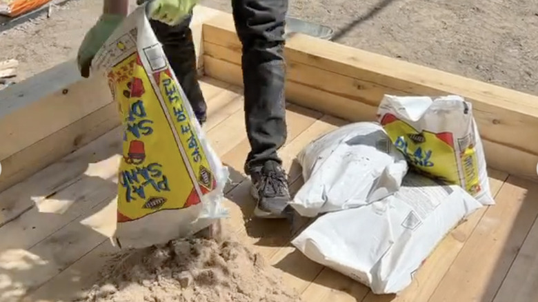 A man pouring sand into an empty wooden sandbox.