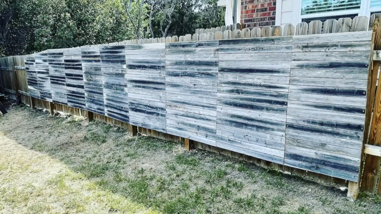 A fence with horizontal distressed wood pallets.