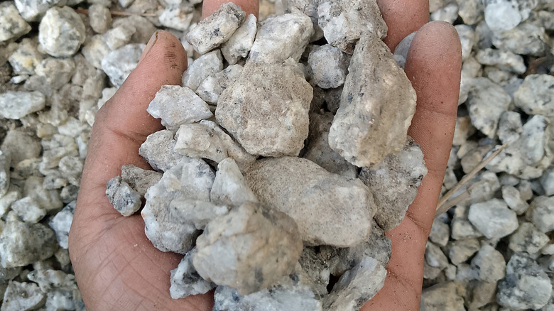 A person holding crushed stone in their hand, with more crushed stones in the background