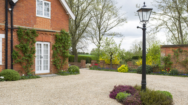 A gravel driveway with a lamppost in the center in front of a cute brick house