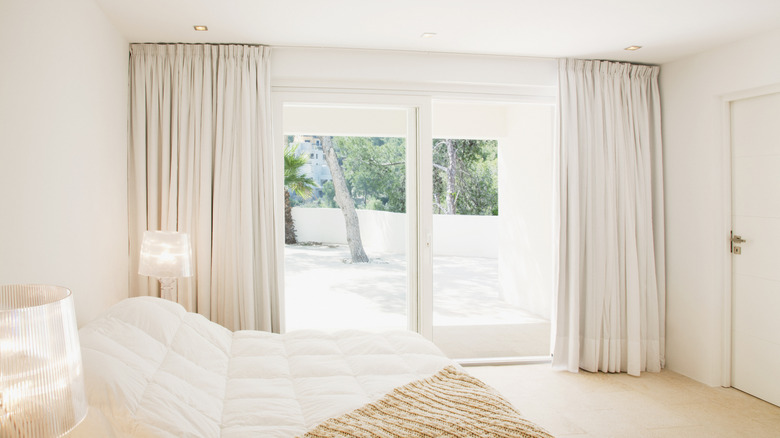 View of bedroom with large glass doors and windows with white curtains pulled back