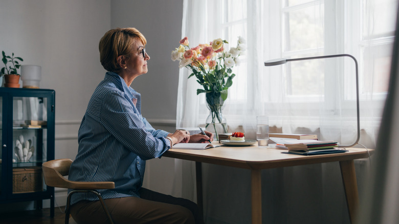 Woman in a home office with light-filtering curtains next to a desk