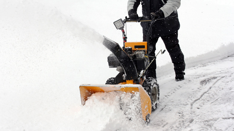 A person pushes a yellow snow blower through several inches of snow.