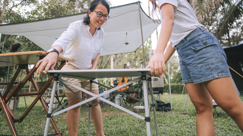 Two women setting up short folding table for an outdoor picnic