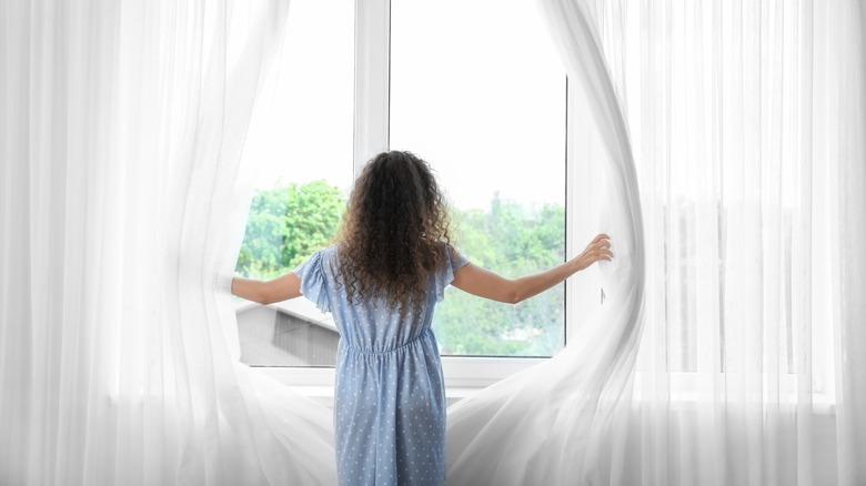 woman opening white window curtains