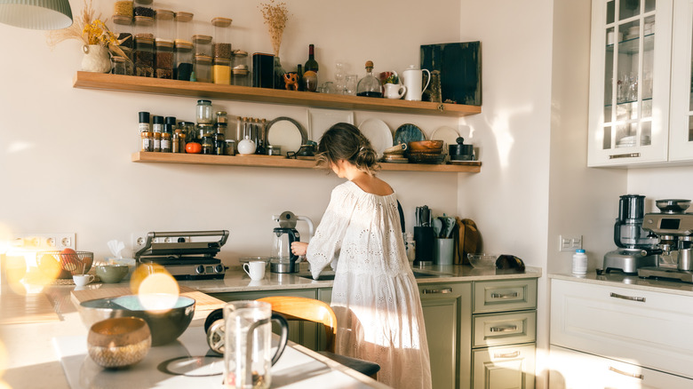 Woman standing at crowded kitchen countertop.