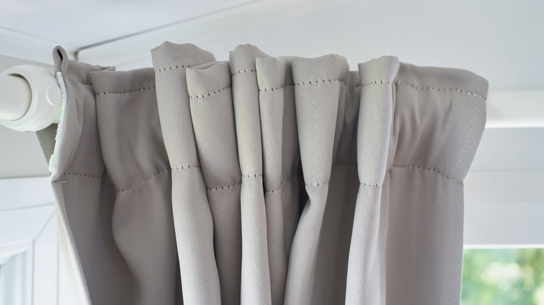 A grey curtain on a white rod, bunched up in a corner