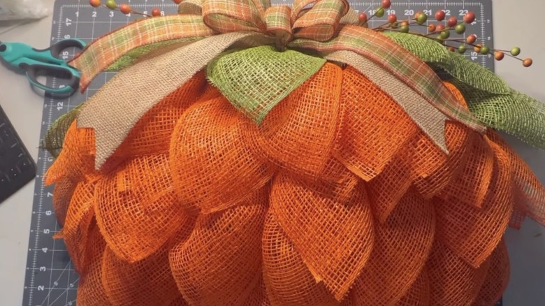 A pumpkin wreath made out of burlap mesh adorned with decorative ribbon