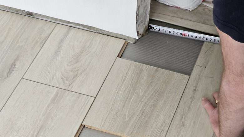 A handyman measuring a corner to lay down laminate tiles