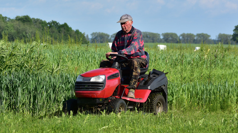 A man cutting long grass with a ride-on rotary mower