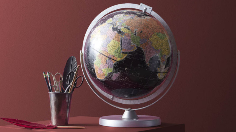 An oxblood red well behind a globe and feather quills