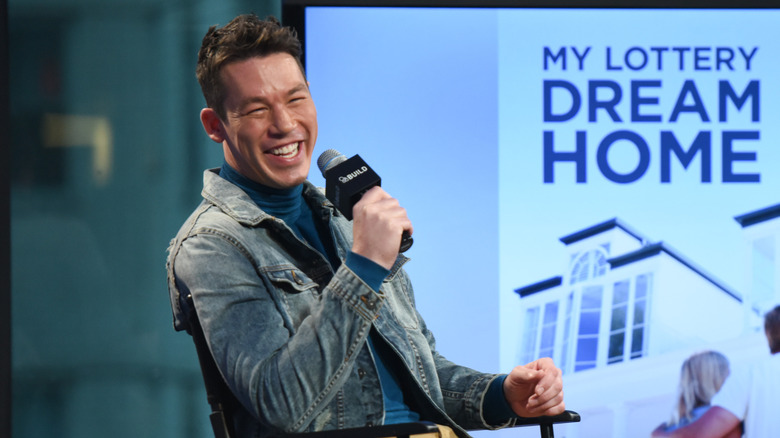 David Bromstad laughing into a microphone at the AOL Build Speaker Series, with a poster of My Lottery Dream Home in the back