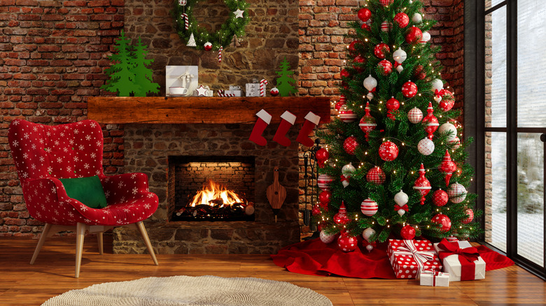 Red and green Christmas décor in front of a blazing fire, featuring a Christmas tree, a red chair, and mini stockings