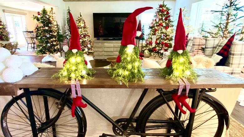 Christmas décor in designer David Bromstad's house with numerous Christmas trees and gnomes wearing santa hats sitting on a wooden table on top of a bicycle frame
