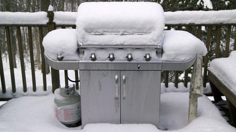 A barbecue and a propane tank covered in snow