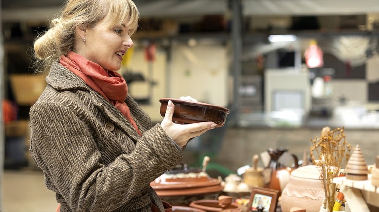 A person smiles as they inspect a brown bowl at a secondhand market