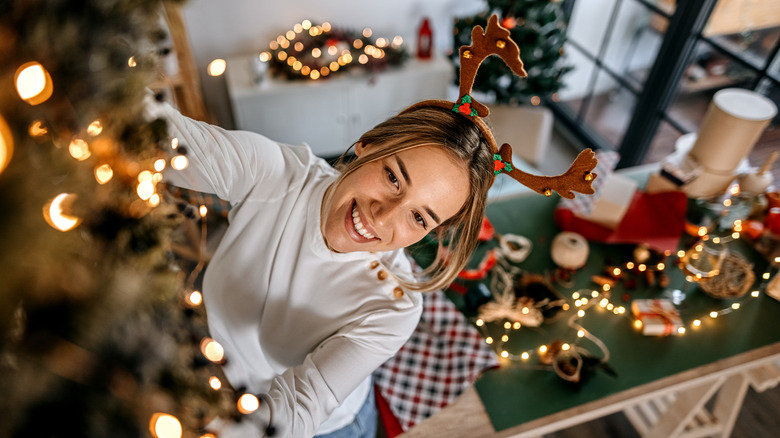A persons wears a reindeer headband while stringing up Christmas lights