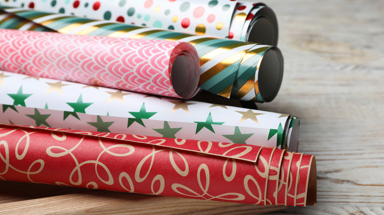 Different colored rolls of Christmas wrapping paper sit on a wooden table