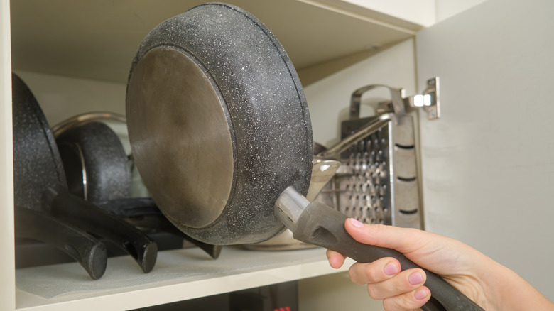 A hand reaching into a cabinet to store pots and pans.
