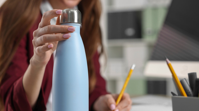 A woman holding a blue metal water bottle at work
