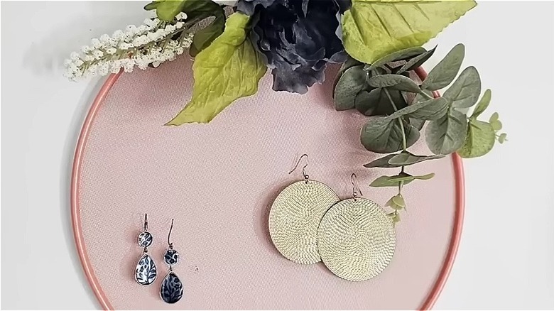 A decorated mesh strainer holding two pairs of earrings