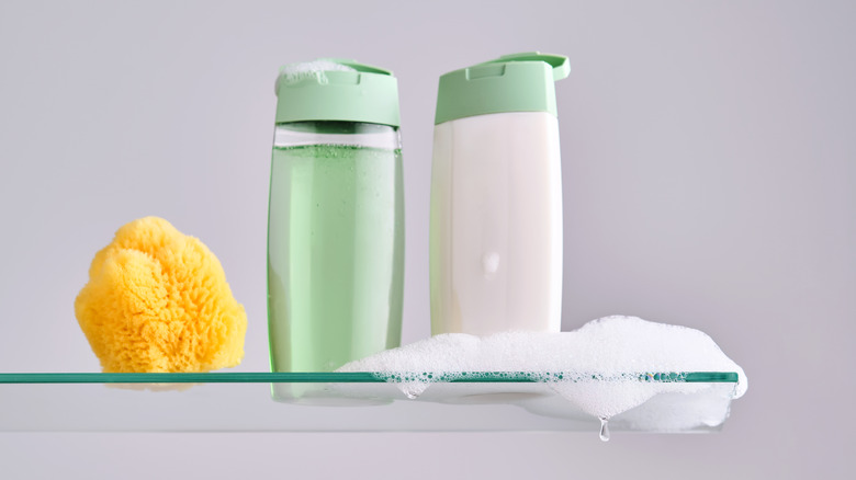 A loofah and a set of green and white shampoo bottles with bubbles.