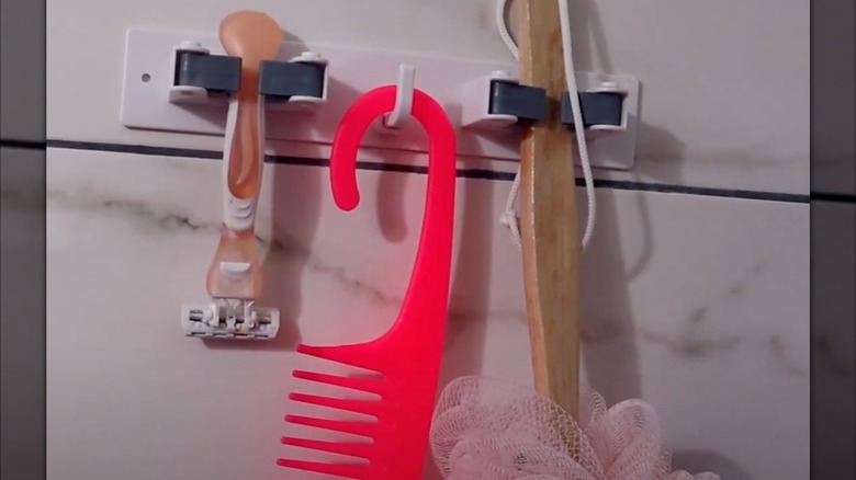 Closeup of a broom holder mounter inside a shower, holding a razor, comb, and loofah