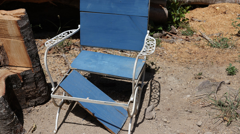 A seat board is broken out of a blue lawn chair