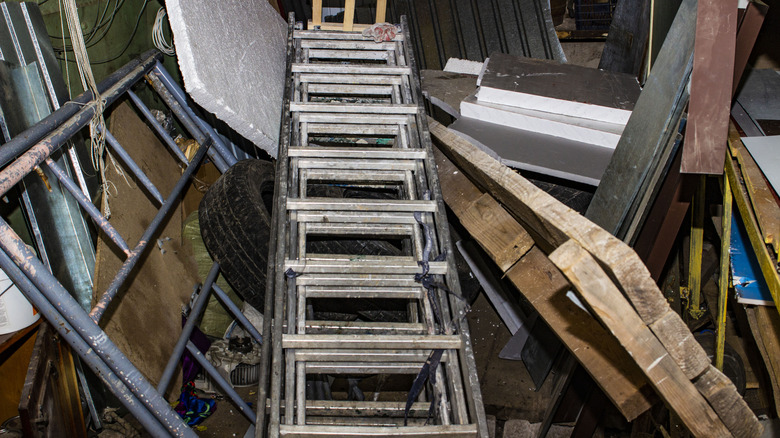 Old ladders are discarded on top of a pile of junk in a garage