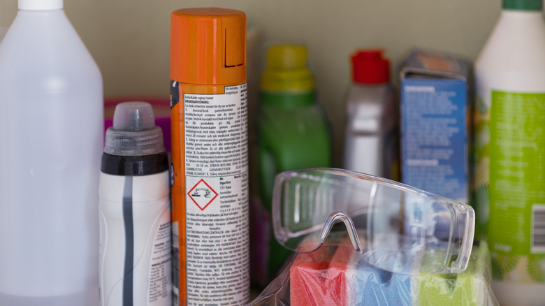 A pair of safety glasses sits on top of sponges next to an assortment of chemical cleaners