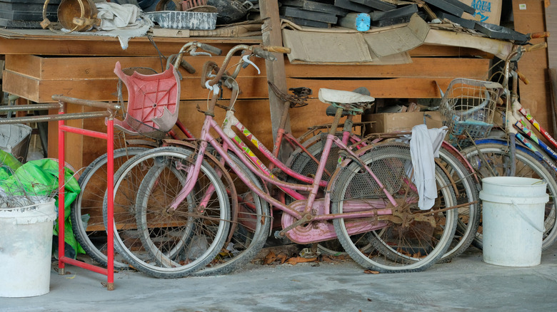 Three old rusty bicycles lean against a wooden chest in a dusty garage